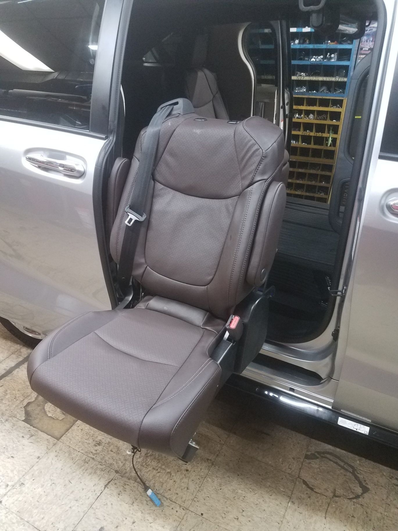 A brown leather seat is sitting in the back of a silver minivan.