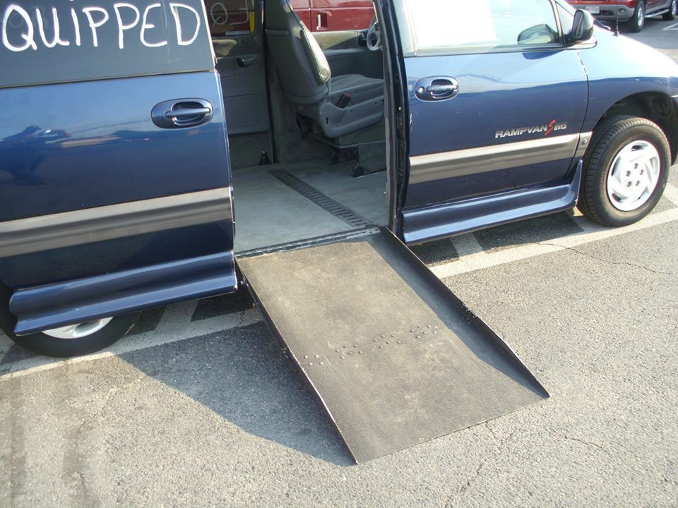 A blue van with a ramp that says quipped on it