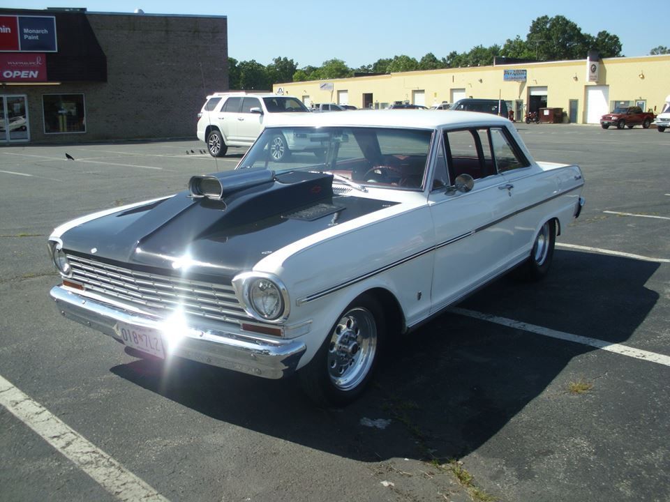 A white car with a black hood is parked in a parking lot