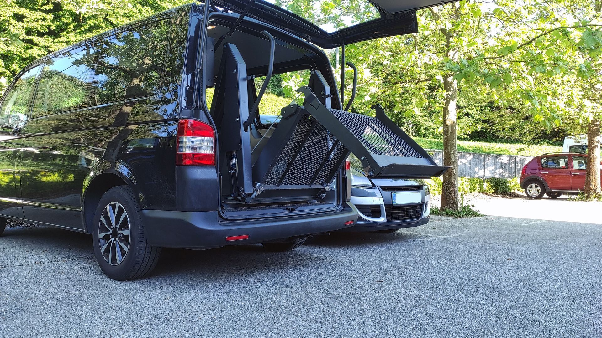 A Black Van With the Back Door Open is Parked Next to a Red Car