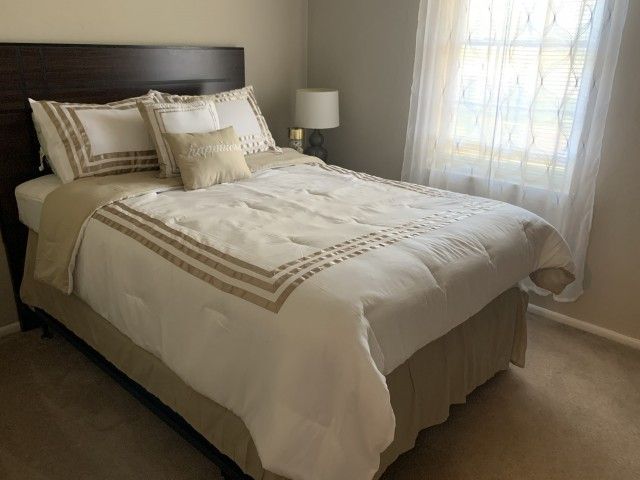 Bedroom with a large bed, bedside lamp, and window with sheer curtains.