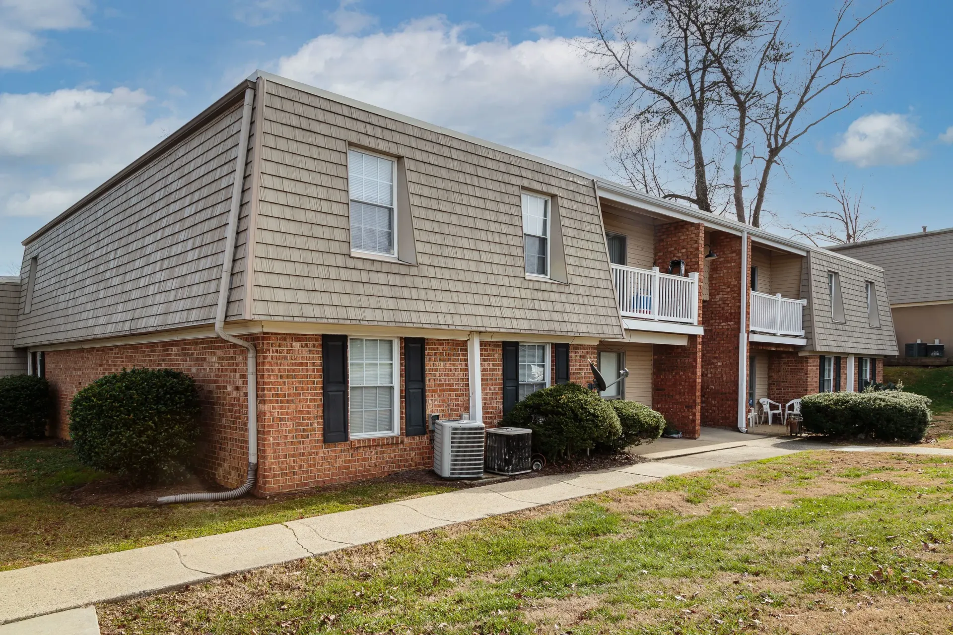Apartment building with brick exterior, brown roof, and balconies at New Irving Heights, which offers apartments for rent in Greensboro, NC. Green shrubs and grass in front.