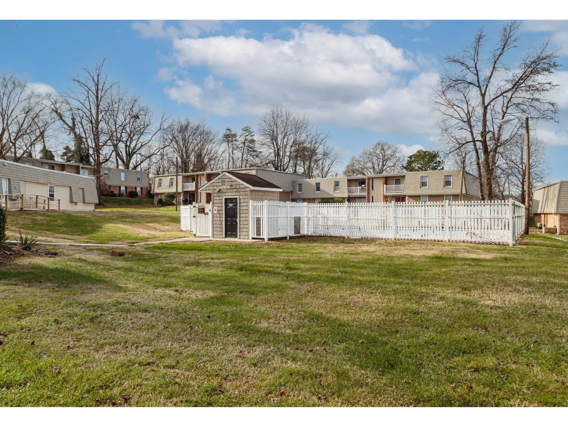 Shared outdoor pool area enclosed by a white fence within an apartment community.