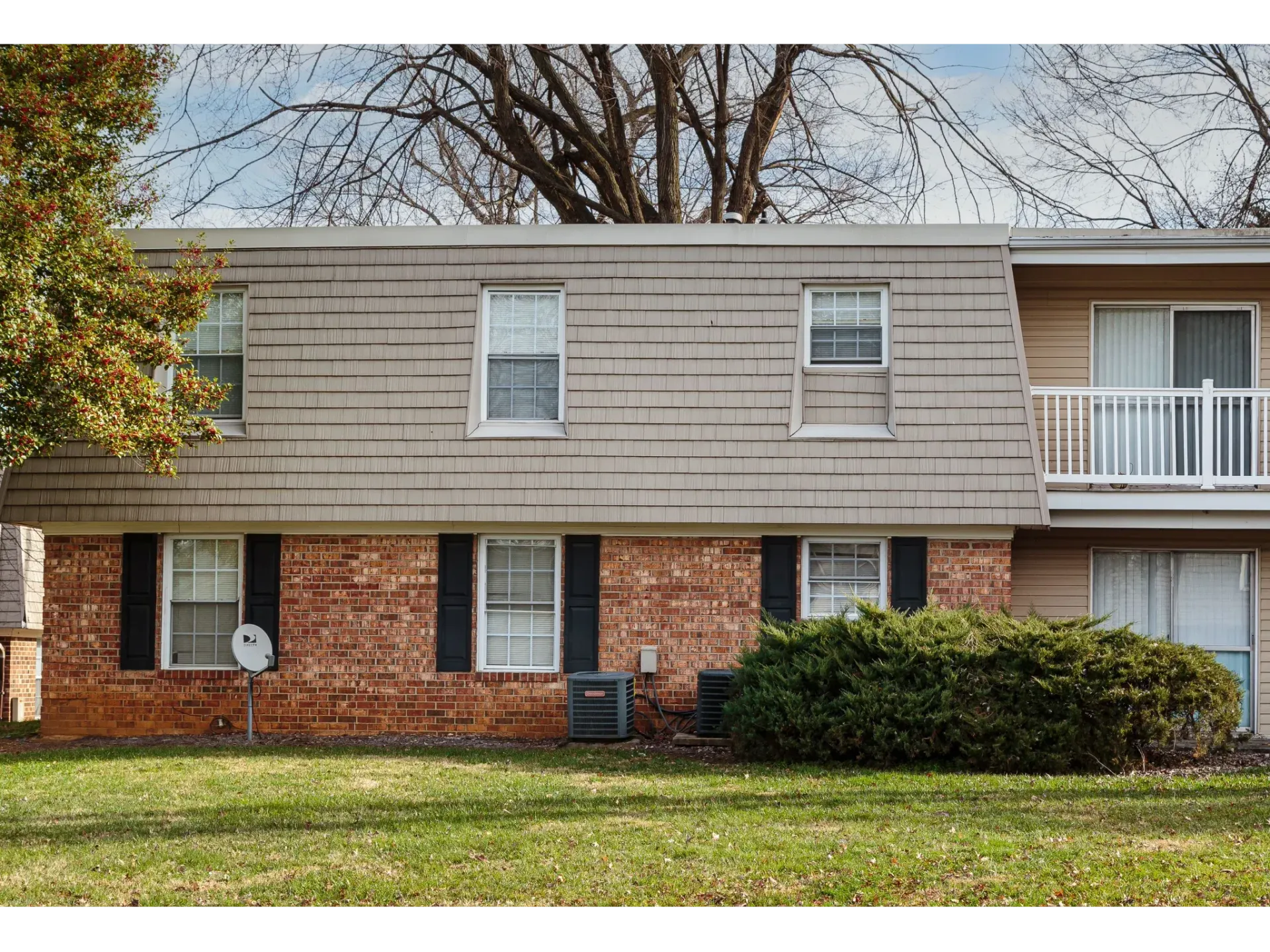 Exterior of a two-story brick-and-beige apartment building with windows and landscaping.