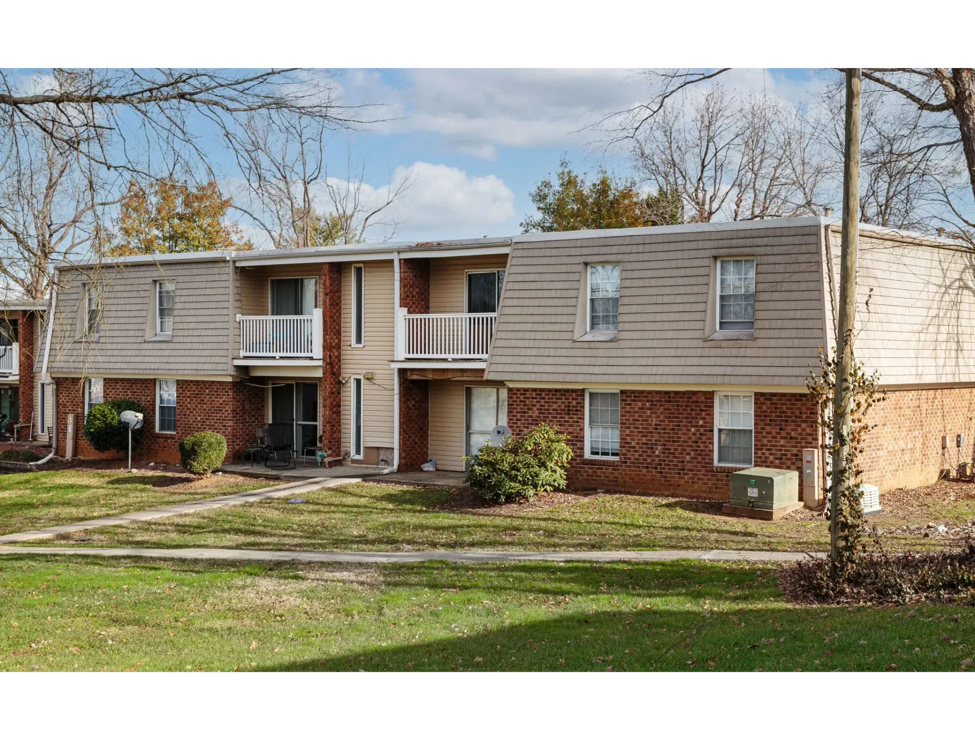 Exterior view of a two-story apartment building with brick base, beige siding, and small balconies.