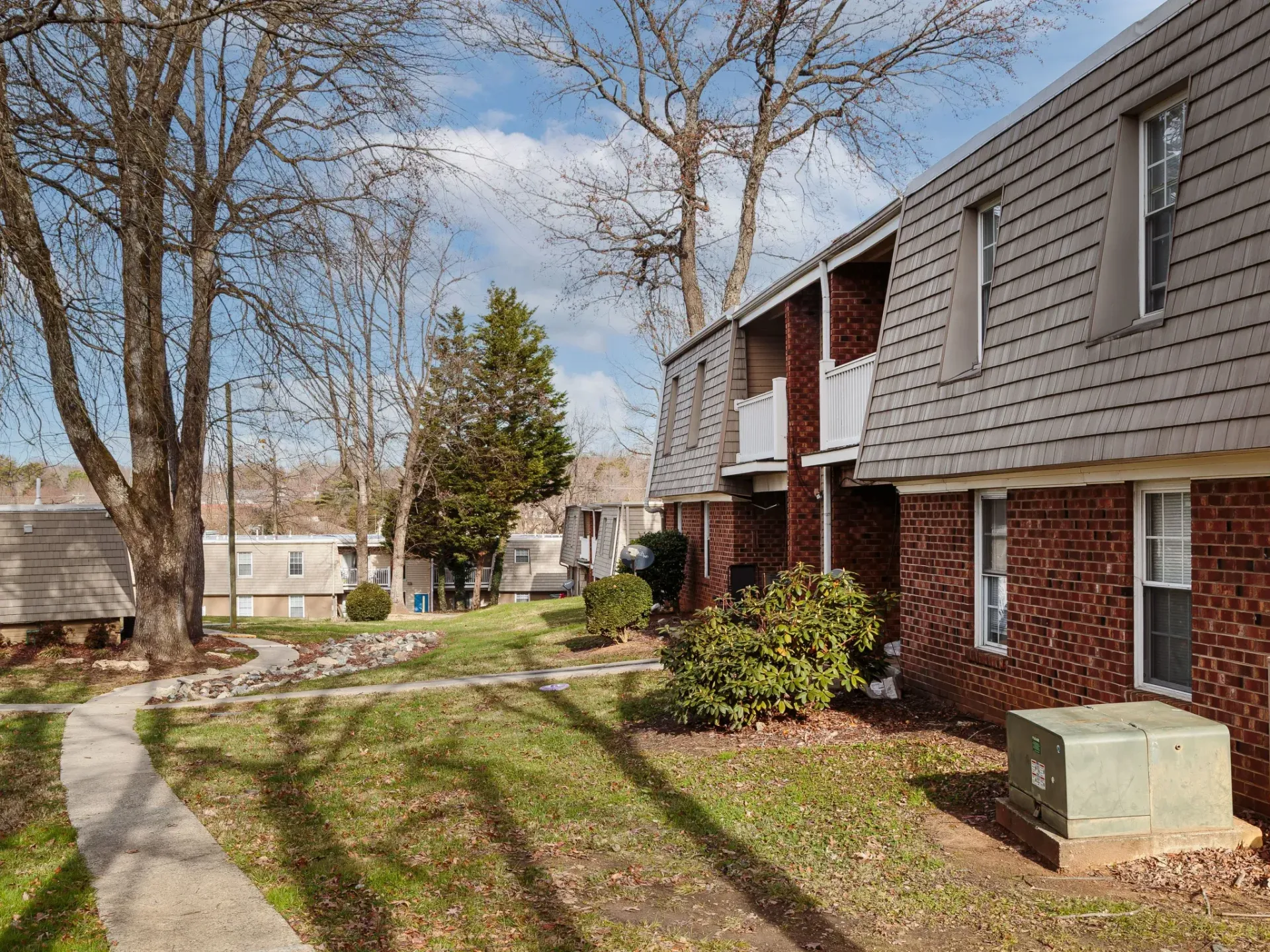 Exterior view of brick apartment building with walkway, trees, and lawn.