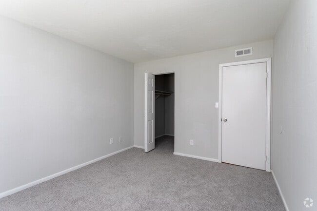 Empty bedroom with gray carpet, white walls, closet, and door at New Irving Heights, which offers pet-friendly apartments for rent in Greensboro, NC.