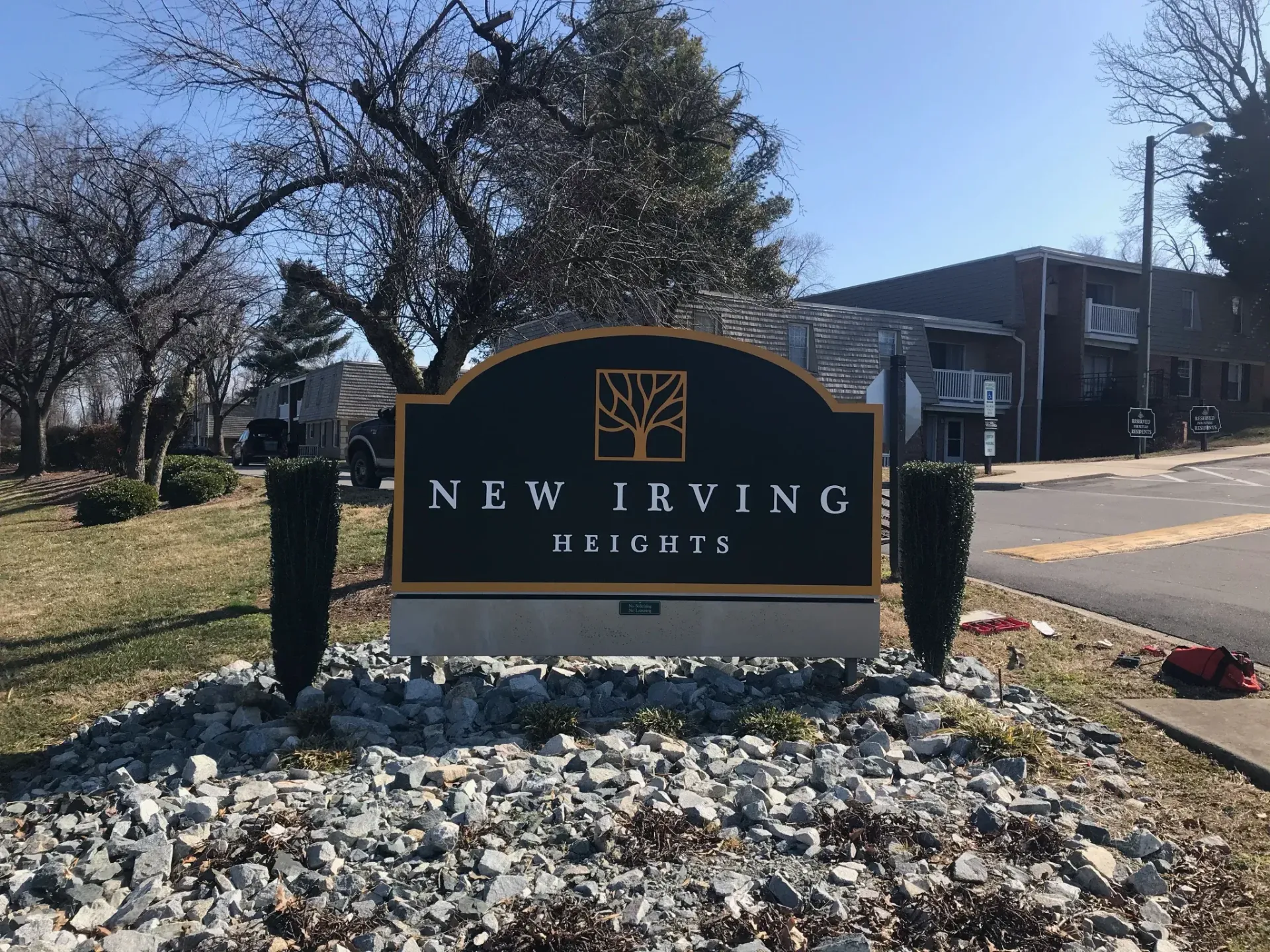 Entrance sign for New Irving Heights apartment community with landscaped rocks and shrubs.