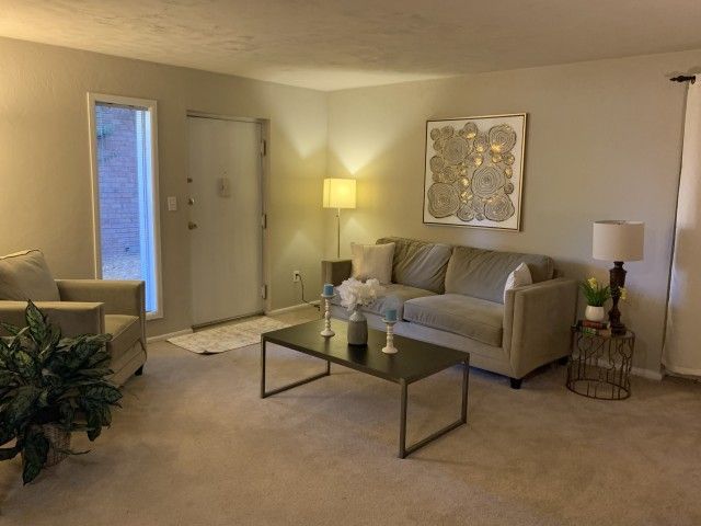 Living room in an apartment with a beige sofa, coffee table, lamps, and wall art.