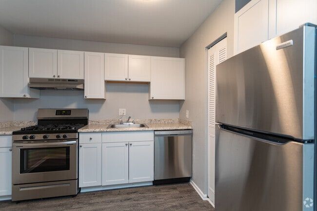 White kitchen with stainless steel appliances, granite countertops, and wooden floors at New Irving Heights, which offers apartments near downtown Greensboro, NC.