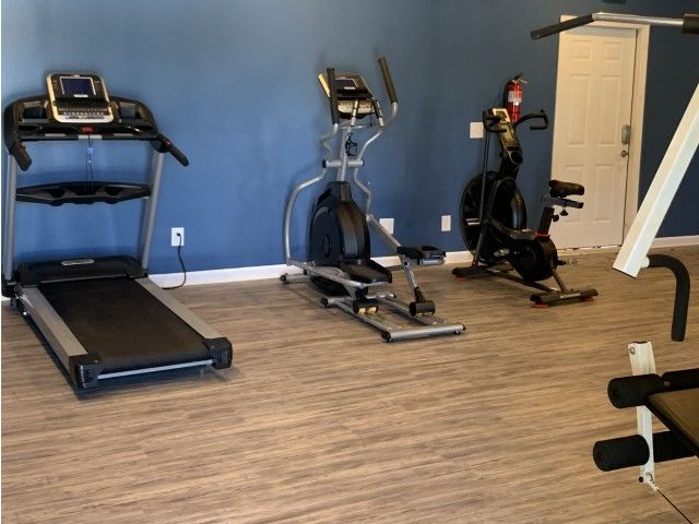 Blue-walled community gym with treadmill, elliptical, stationary bike, and weights.