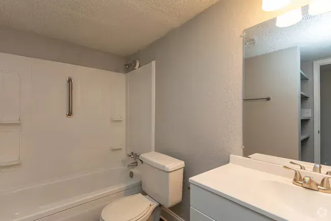 Bathroom with white tub, toilet, vanity, and gray walls at New Irving Heights, which offers pet-friendly apartments for rent in Greensboro, NC.