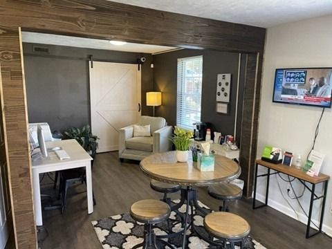 Interior of a modern apartment living area with a round dining table and stools, a sofa, and a wall-mounted TV.