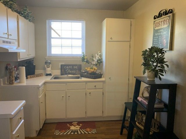 Compact white kitchen with cabinets, a window above the sink, and a small shelf unit to the right.