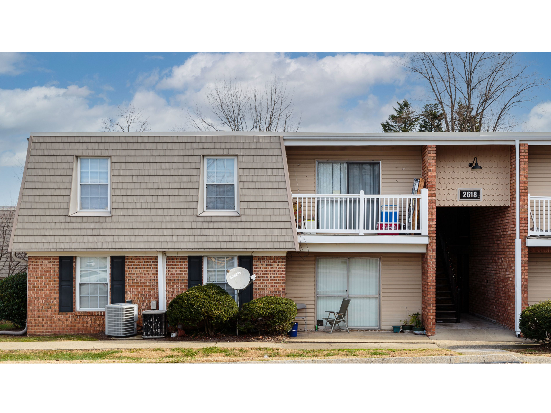 Exterior view of a multi-family apartment building with brick lower level, beige siding, and a second-floor balcony.