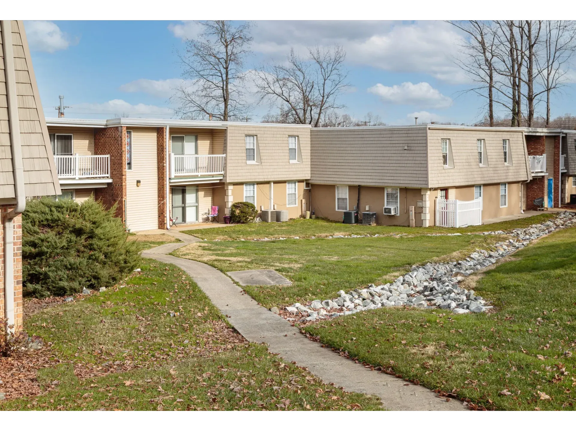 Exterior view of a beige two-story apartment complex with walkway and landscaping.
