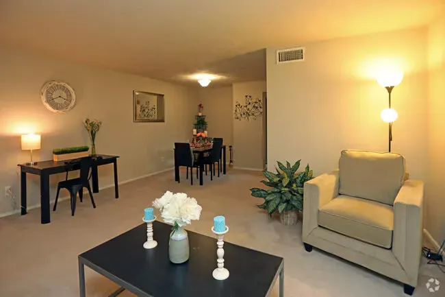 Cozy living room: beige walls, tan armchair, black table and coffee table at New Irving Heights, which offers apartments near downtown Greensboro, NC. Dining area in the background.