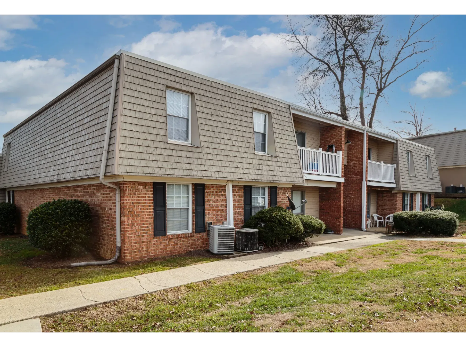 Exterior view of a brick apartment building with a shingled roof and balconies along a walkway.