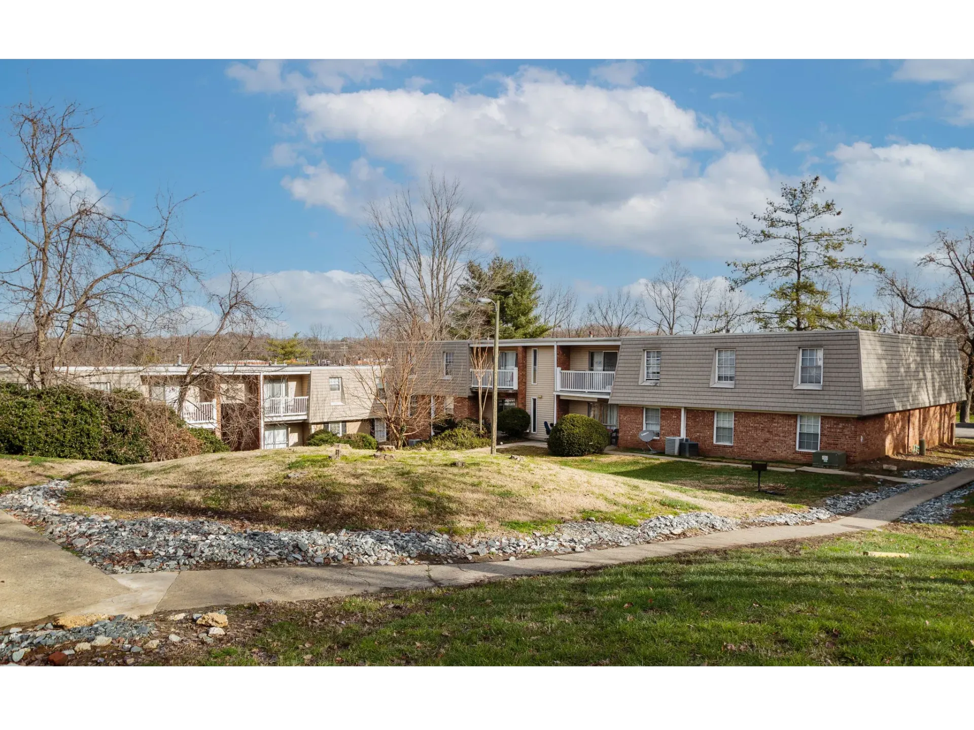 Exterior view of a brick apartment building with lawns, trees, and a walkway.