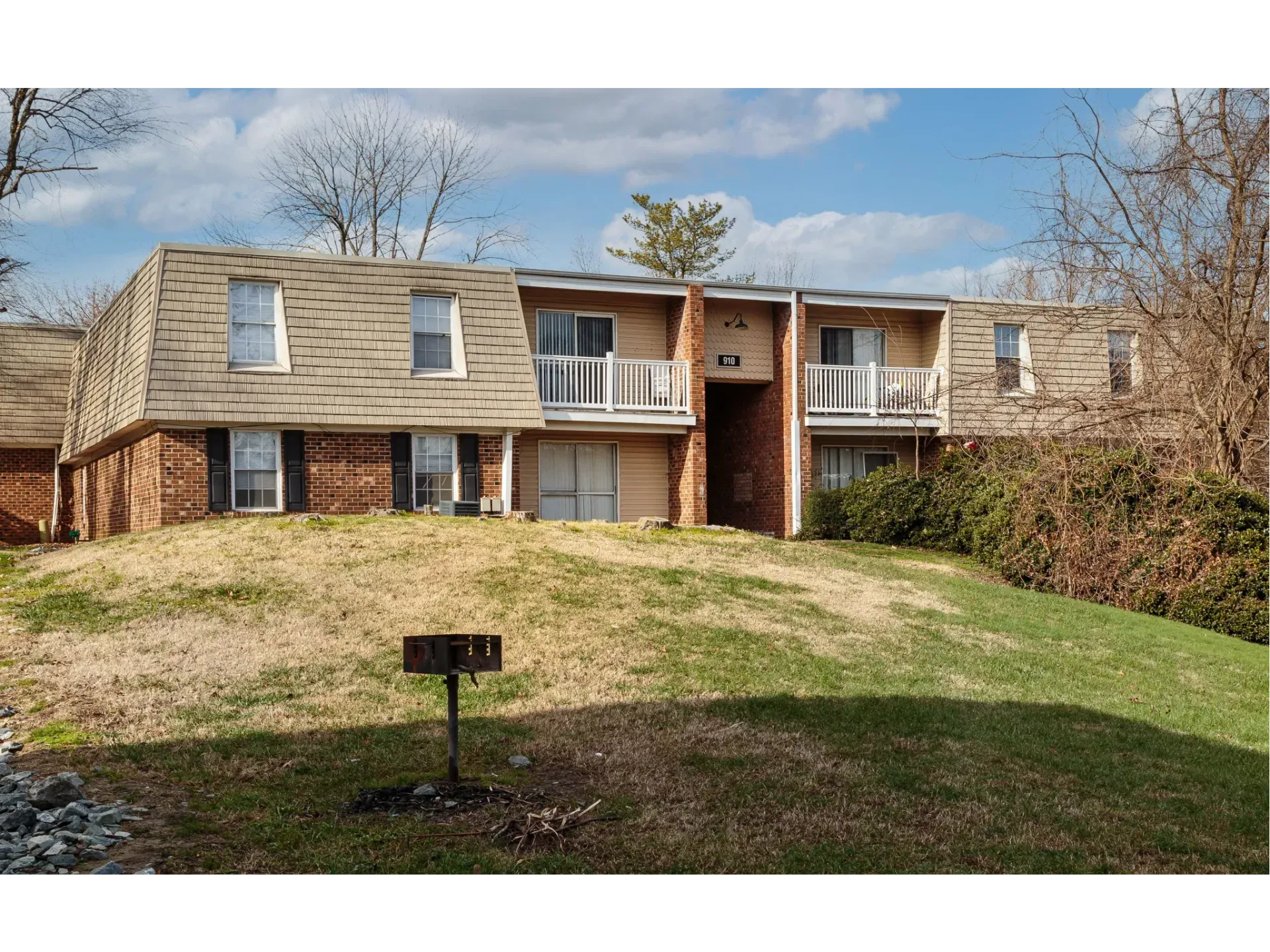 Exterior view of a two-story apartment building with brick ground floor, beige upper siding, and balconies.