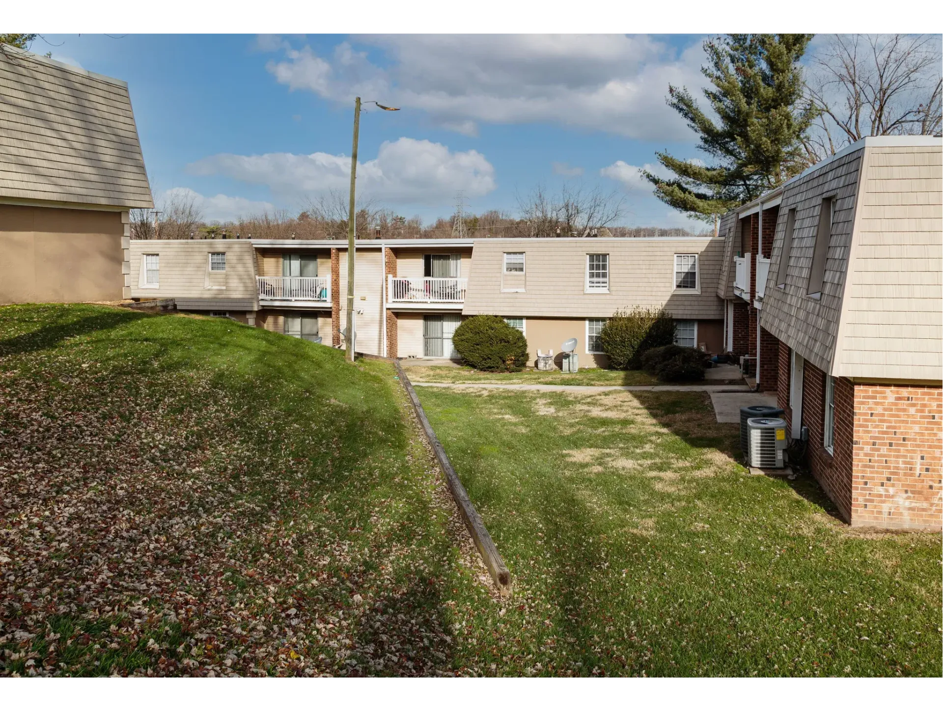 Exterior view of a two-story apartment building with beige siding, balconies, and a grassy courtyard.
