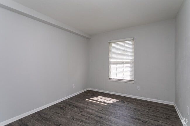 Empty room with gray walls, wood-look floor, and a window with blinds at New Irving Heights, which offers apartments for rent near Downtown Greensboro.