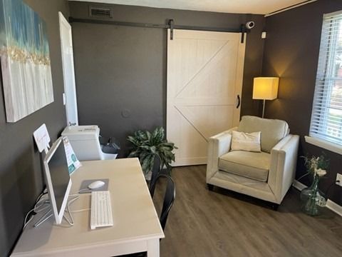 Interior of a modern apartment with a white desk, computer, chair, and a cozy seating area with a sliding barn door.