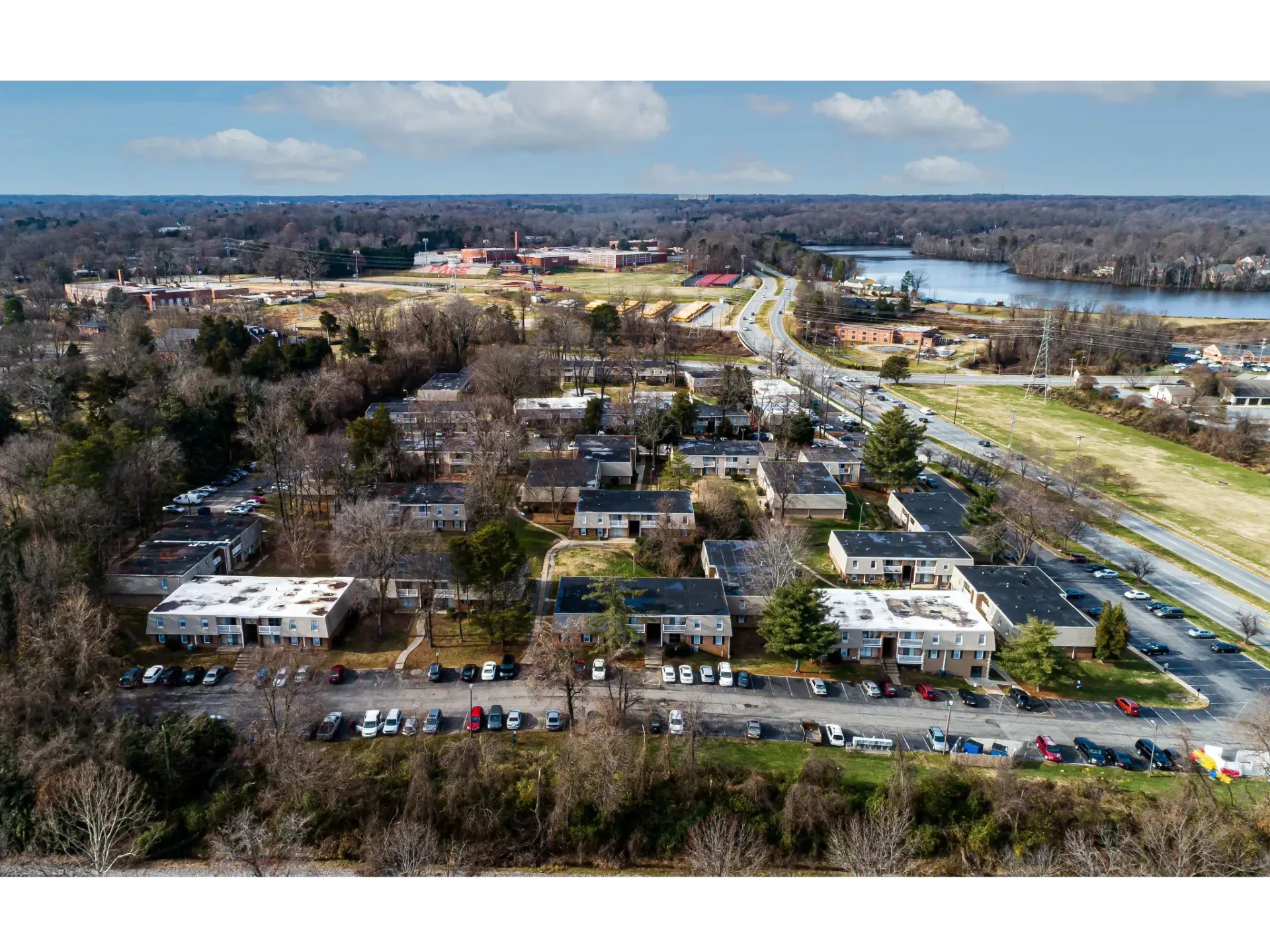 Aerial view of a multifamily apartment community with several buildings, parking lots, and surrounding trees.