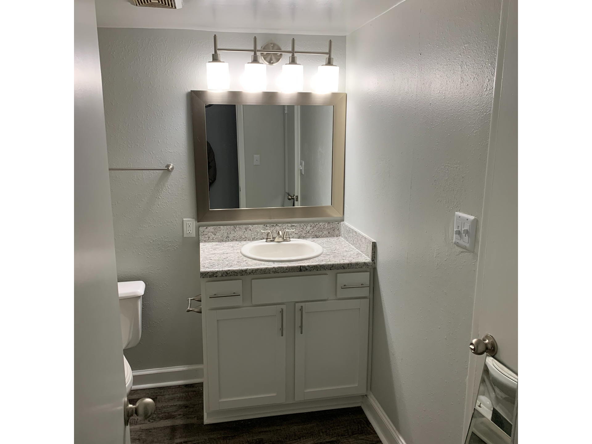 Bathroom vanity with granite countertop, sink, framed mirror, and a four-bulb light fixture.