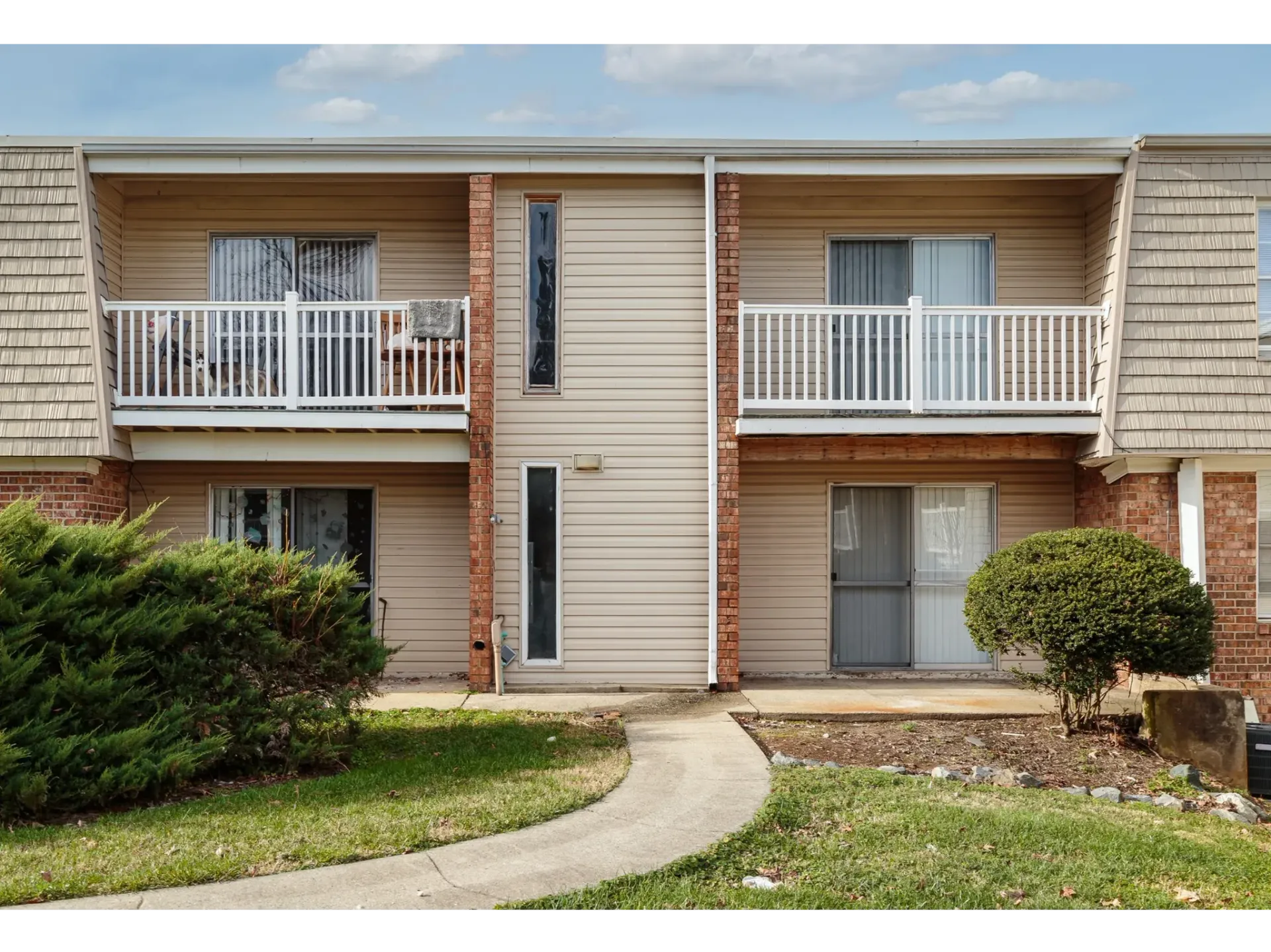 Exterior of a two-story apartment building with beige siding, brick columns, and white balcony rails.