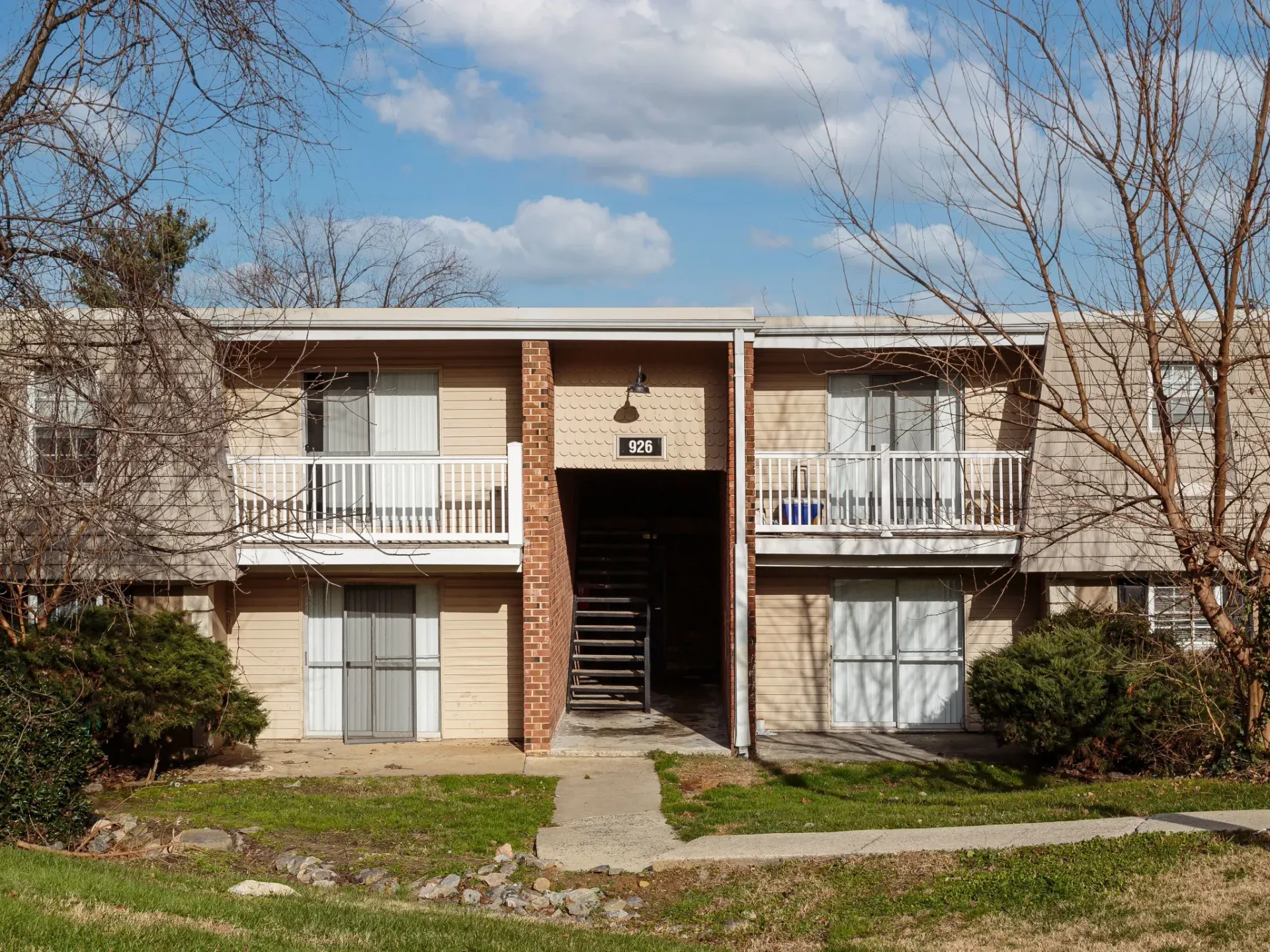 Exterior of a two-story apartment building with a central brick stairwell and white balconies.