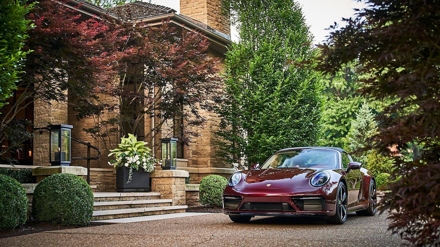 A red sports car is parked in front of a brick house.