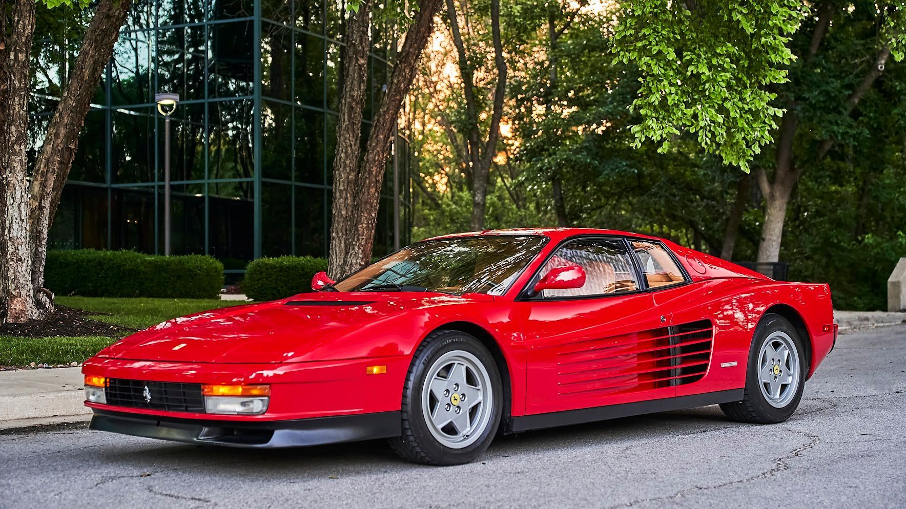 A red ferrari testarossa is parked in front of a building.