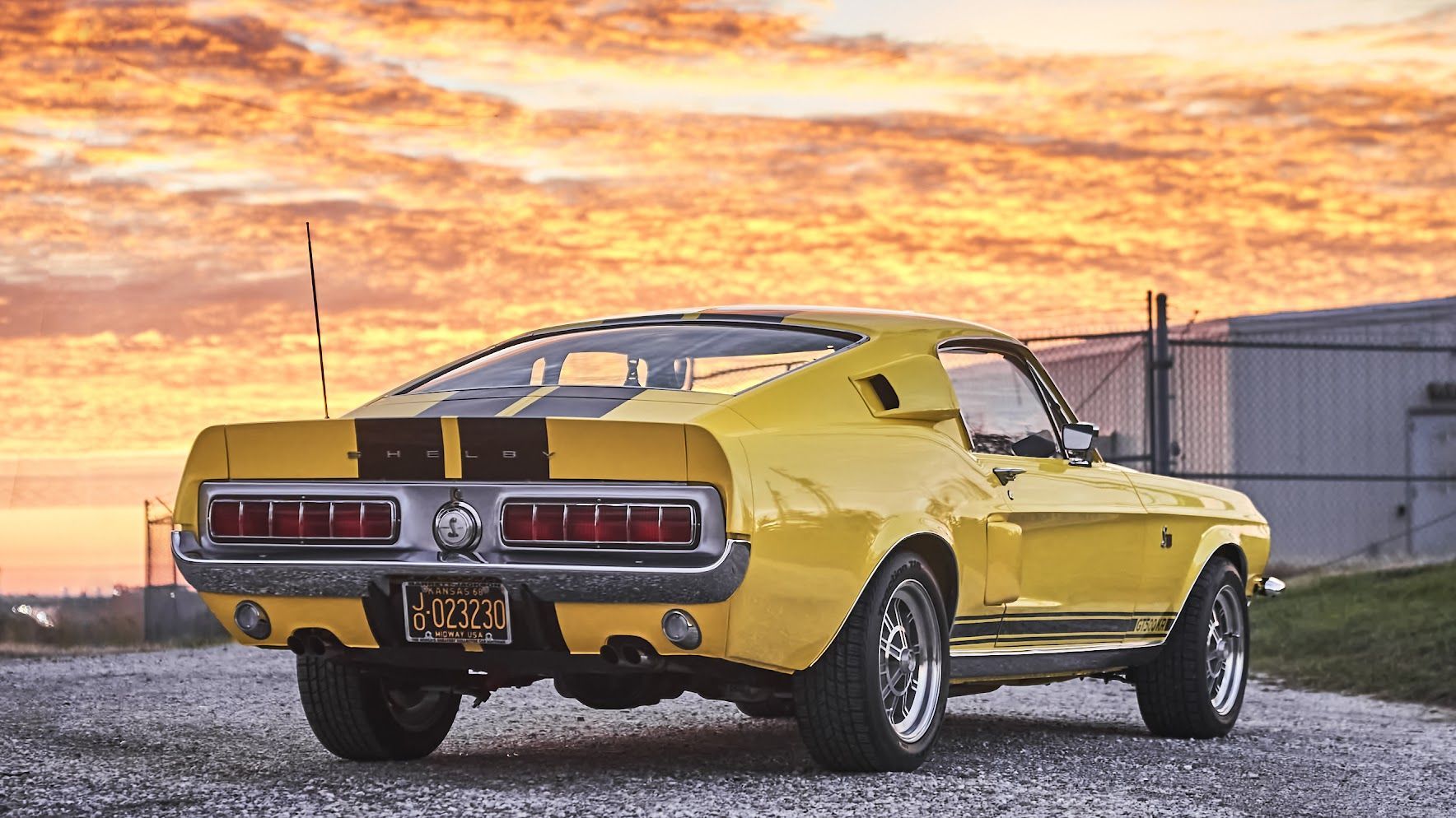 A yellow mustang is parked on a gravel road at sunset.