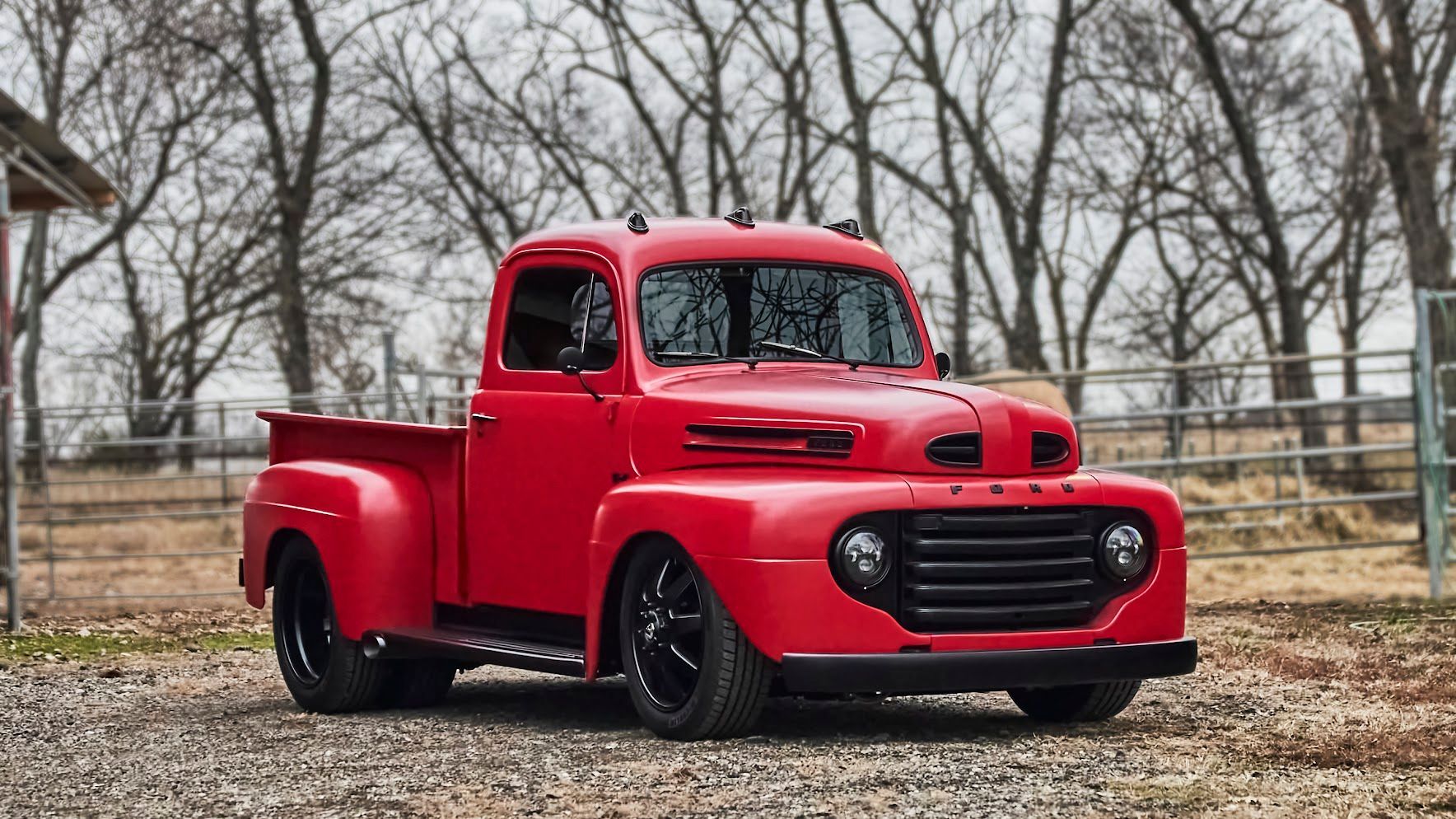 An old red truck is parked in a gravel lot.