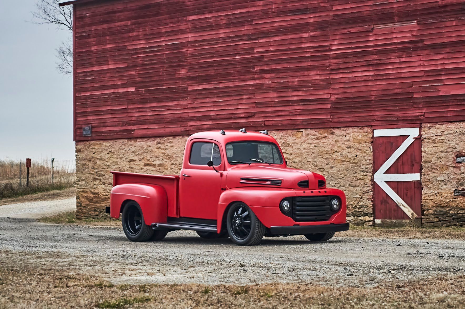 A red truck is parked in front of a red barn.