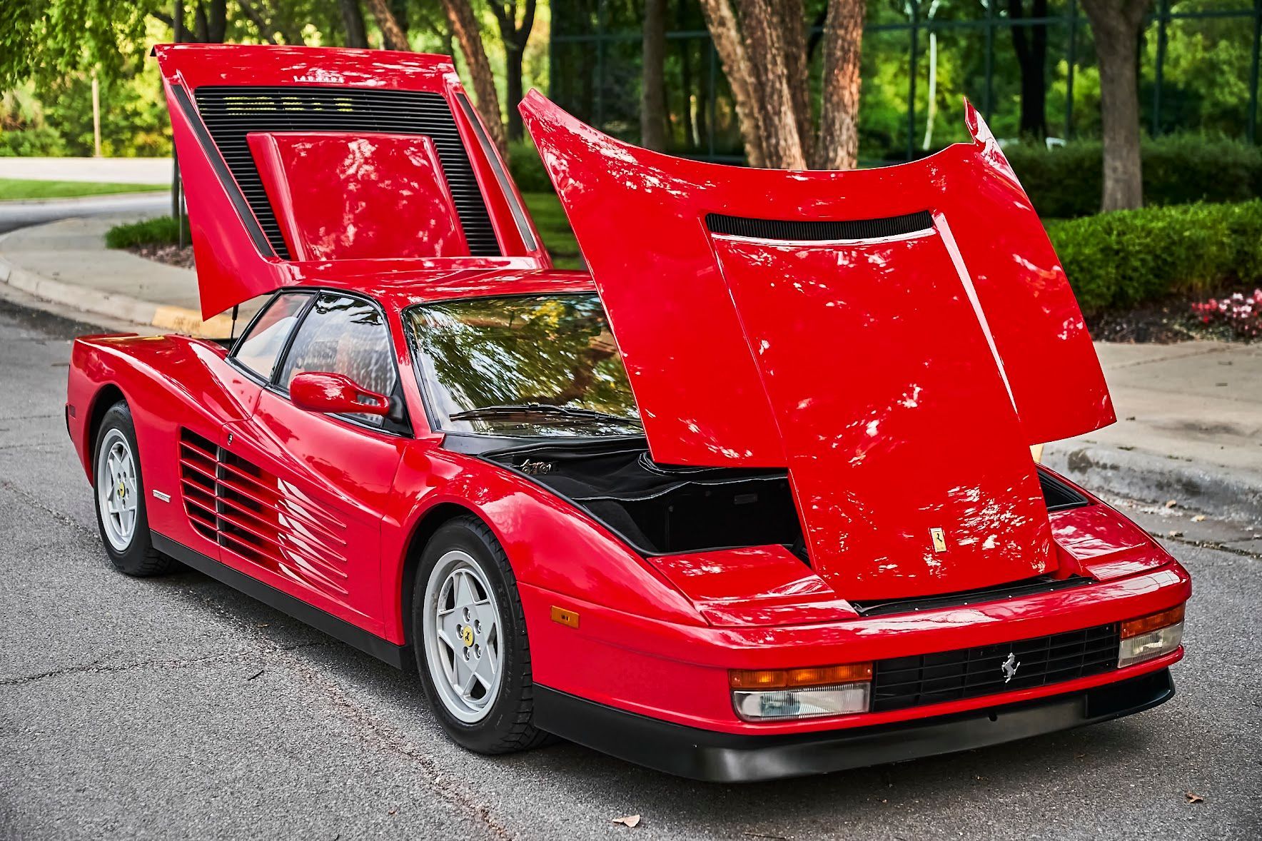 A red ferrari with the hood up is parked on the side of the road.