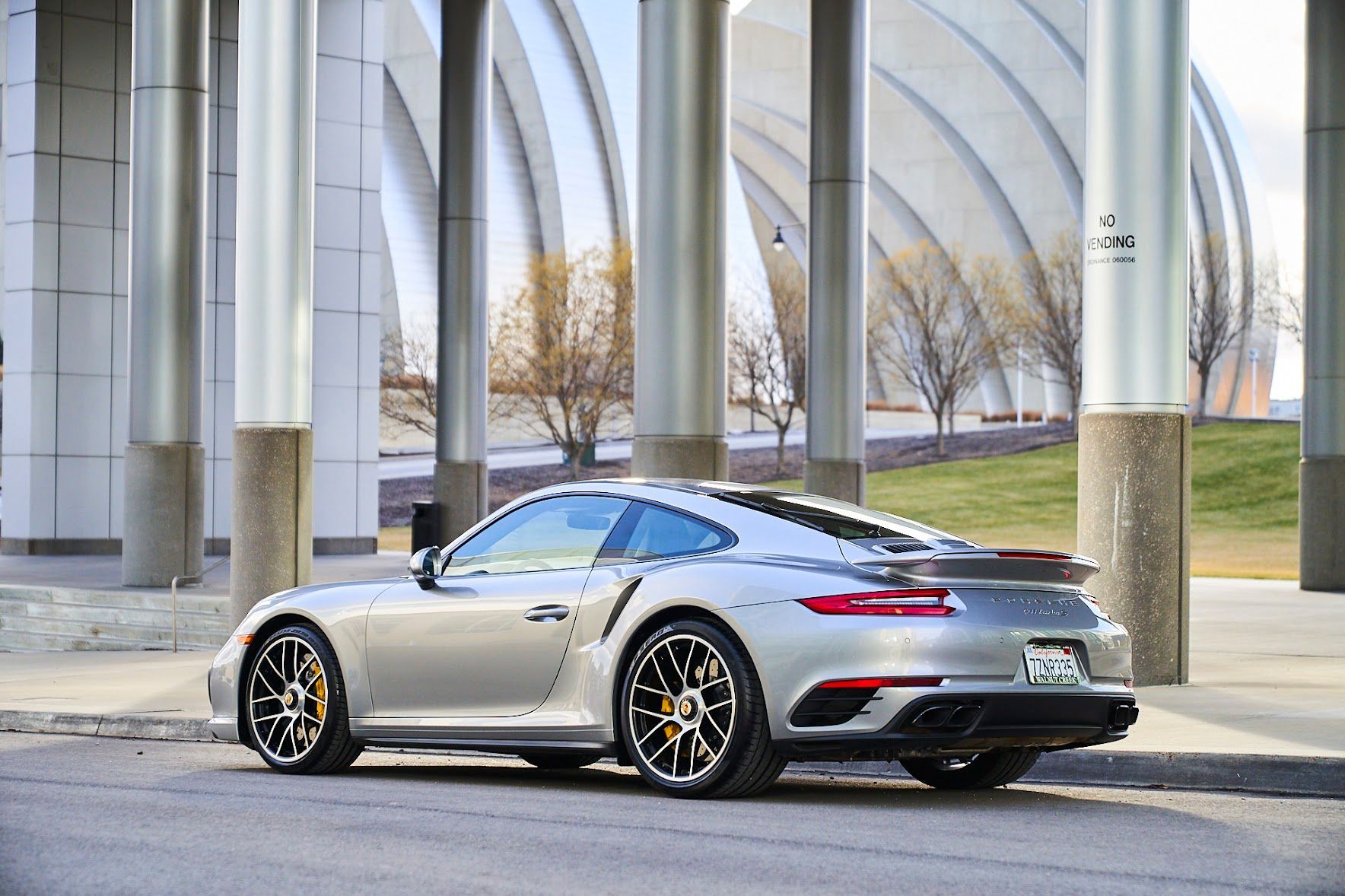 A silver porsche 911 turbo s is parked in front of a building.