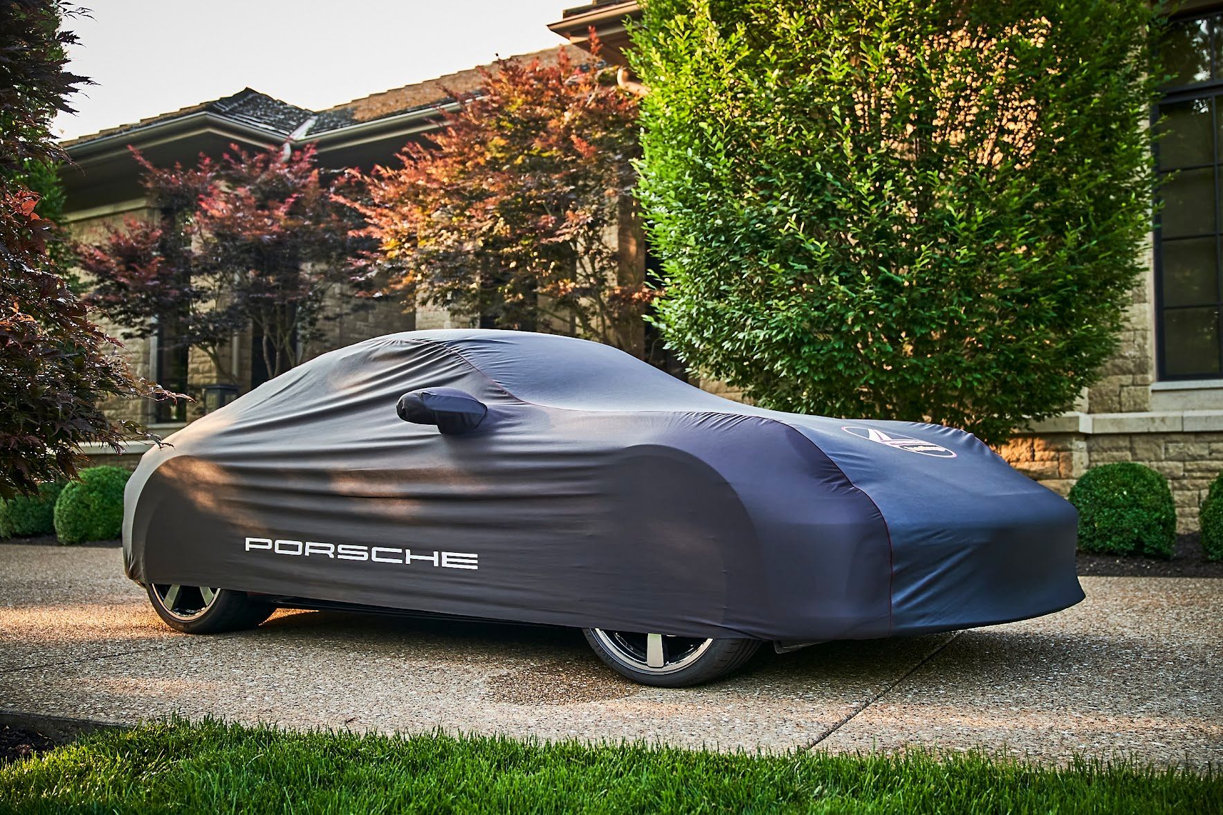A porsche 911 targa car with a cover on it is parked in front of a house.