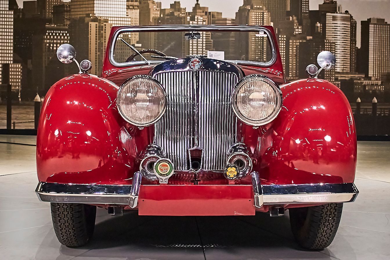 A red car is parked in front of a city skyline.