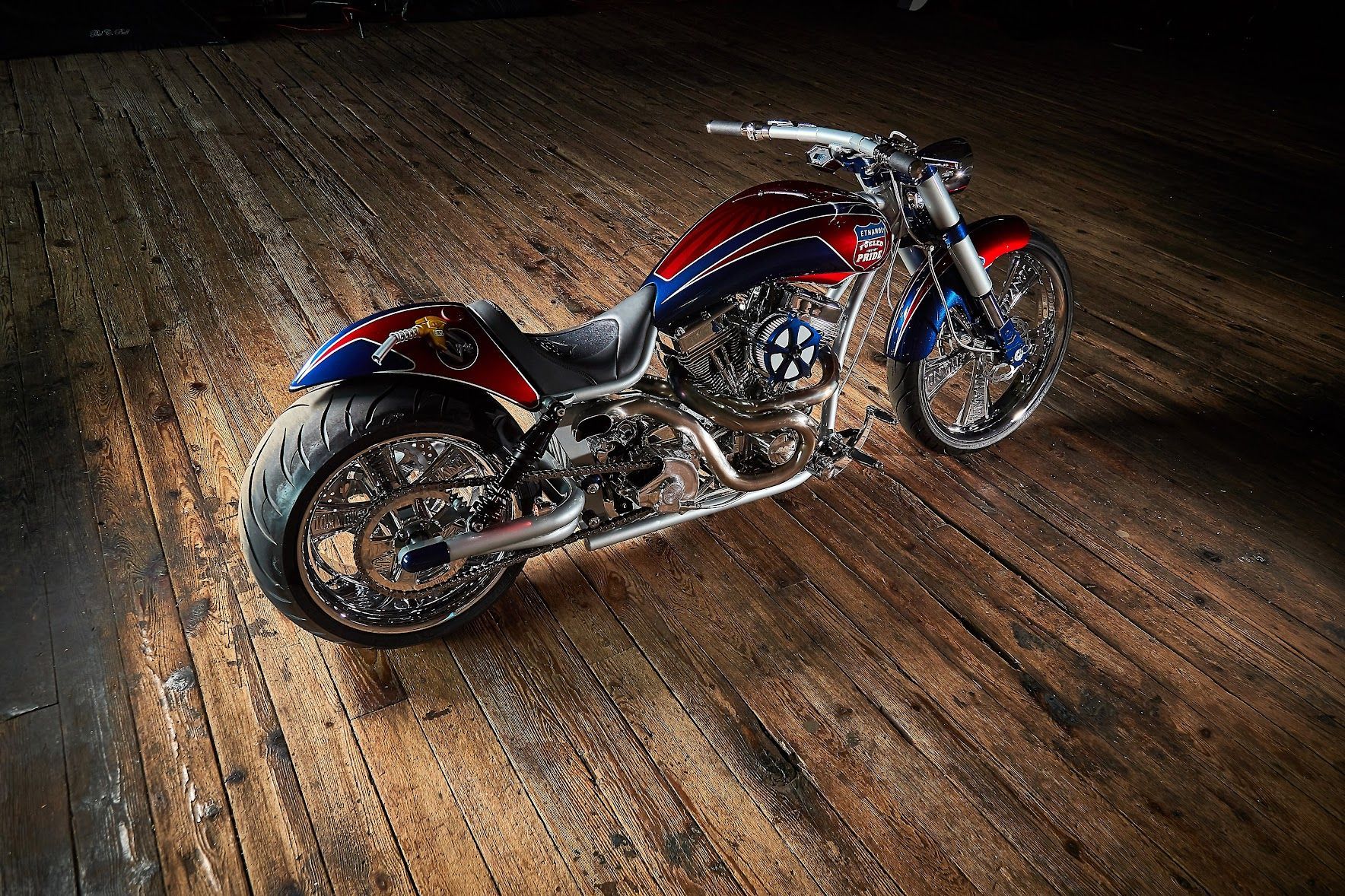 A red , white and blue motorcycle is parked on a wooden floor.
