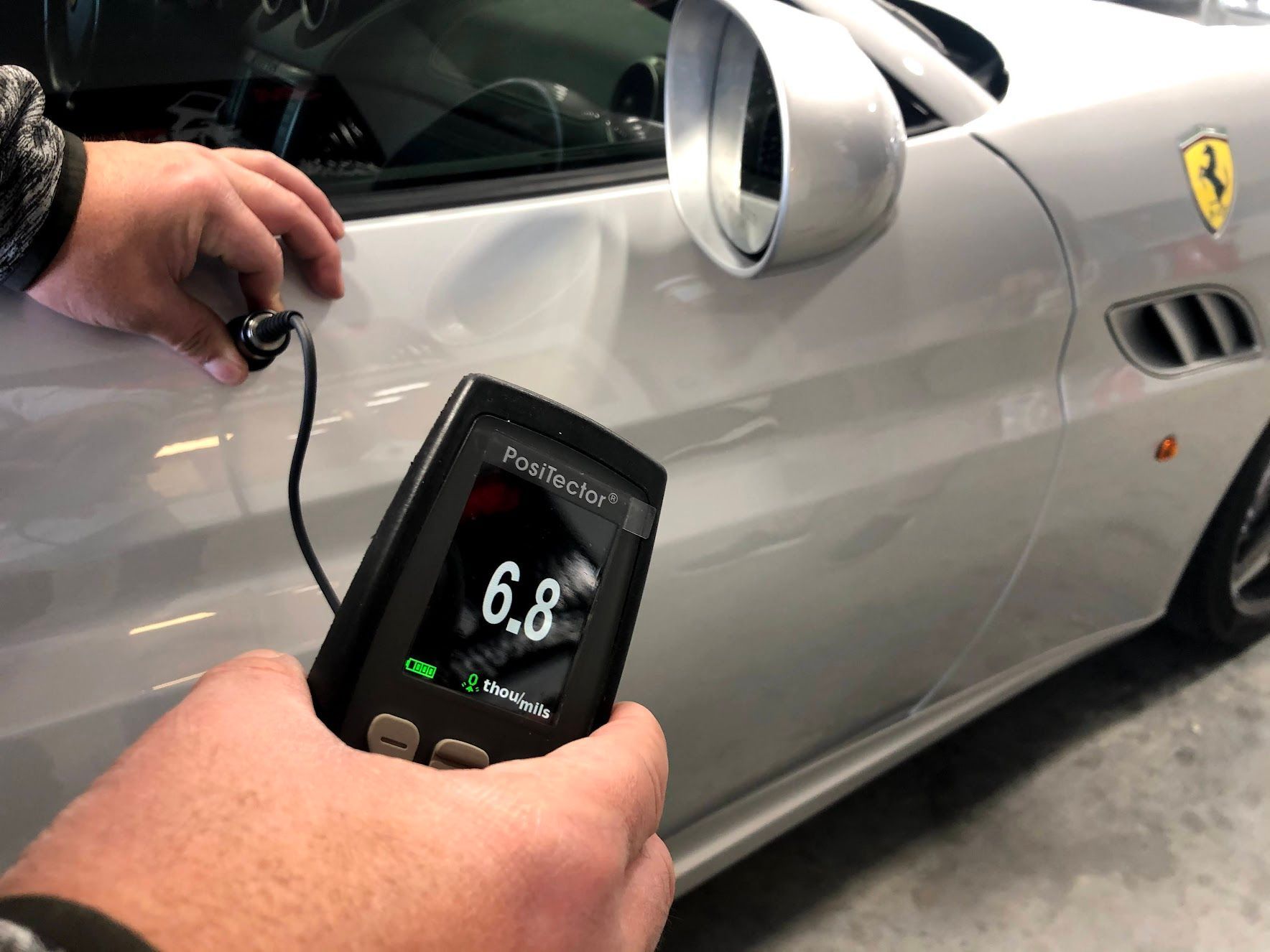 A person is holding a device that says 6.8 on it in front of a car.