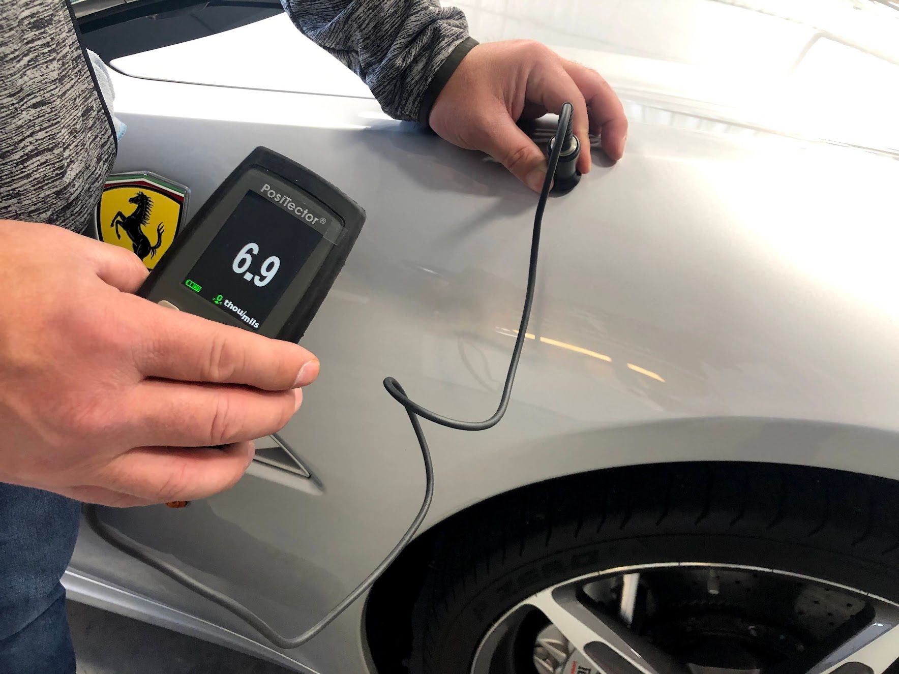 A person is measuring the thickness of a car with a device.