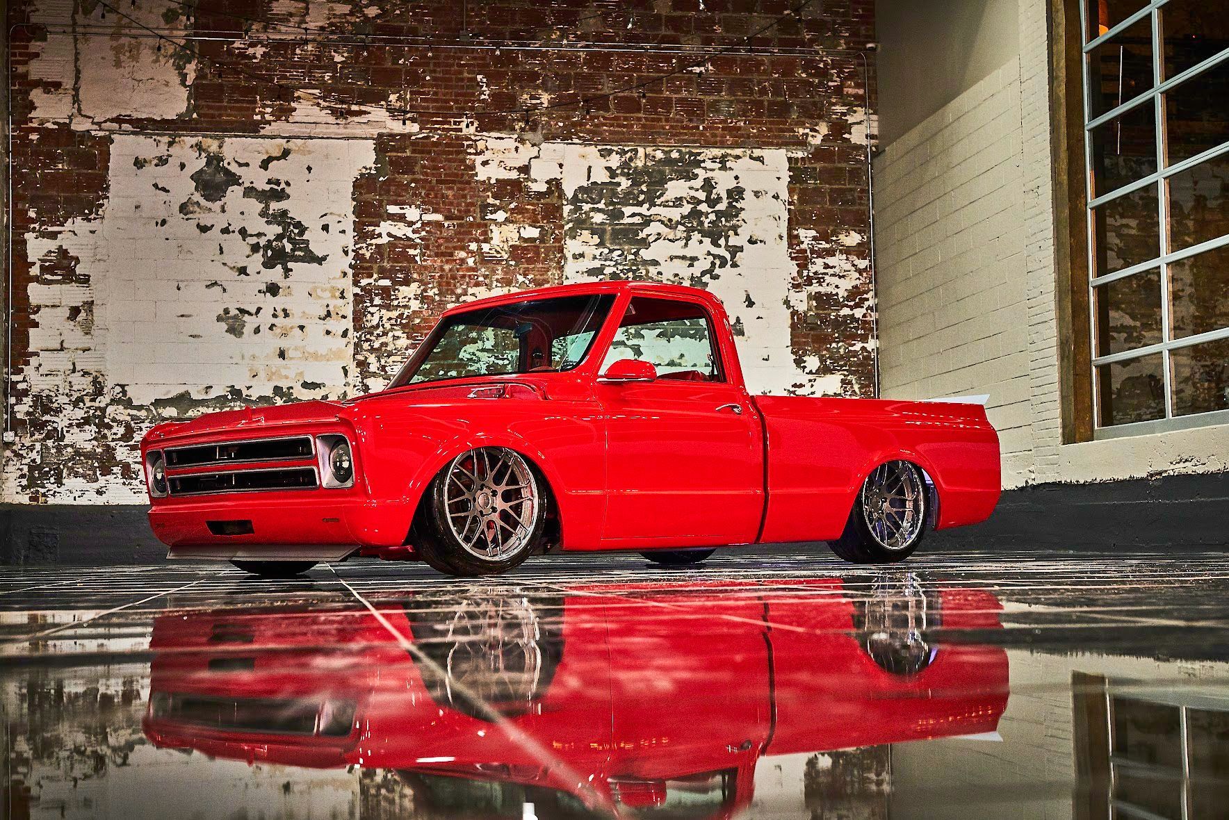 A red truck is parked in front of a brick wall.