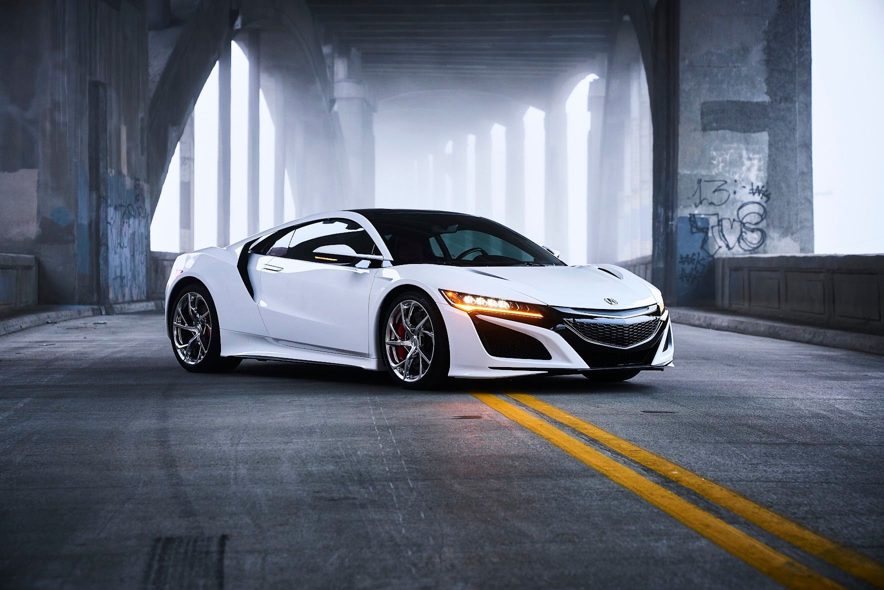 A white sports car is parked on the side of a road under a bridge.