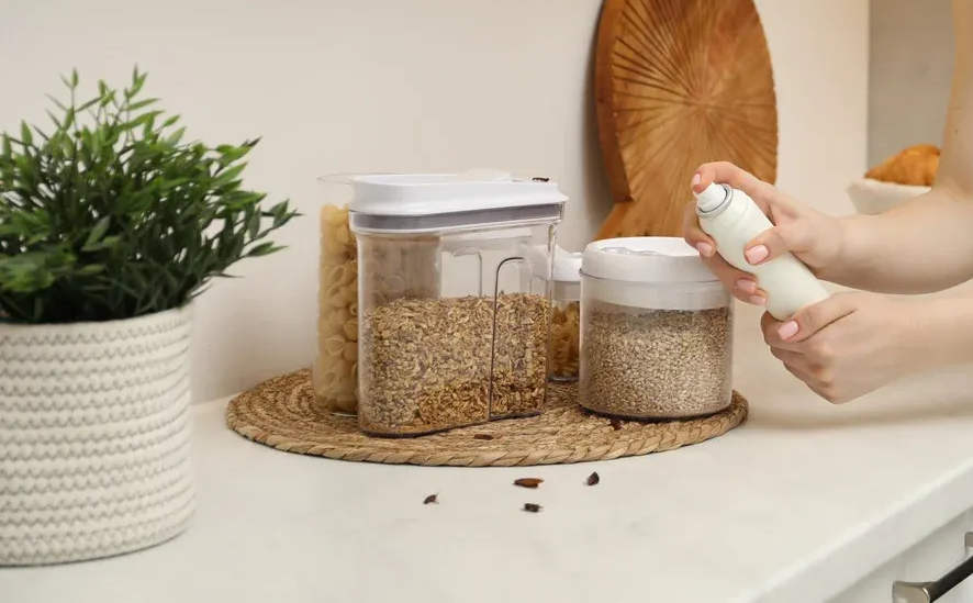 A person sprays a pantry container with white spray in a kitchen.