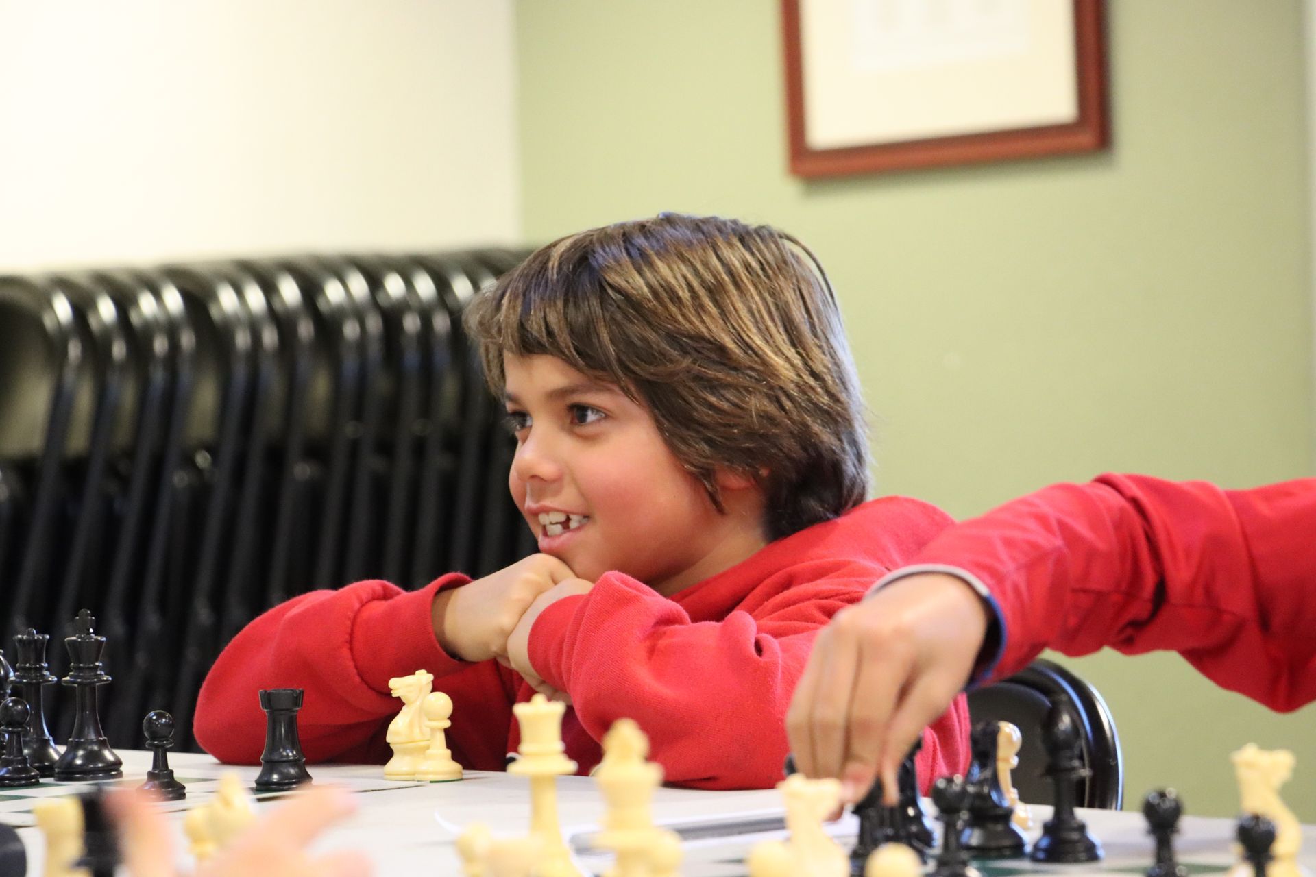 A Montessori child  in a red sweater is playing chess