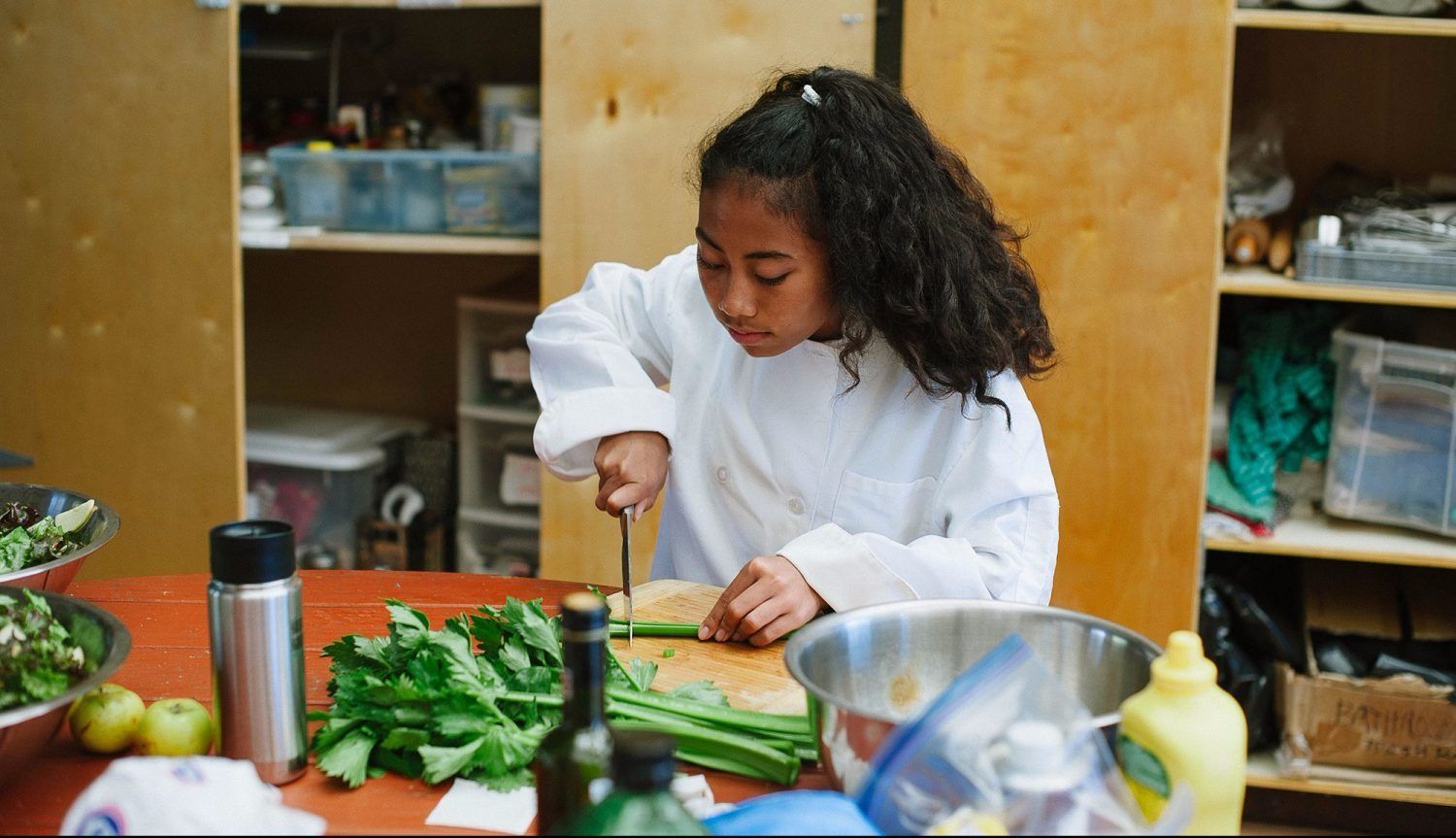 a Montessori child is cutting vegetables on a cutting board