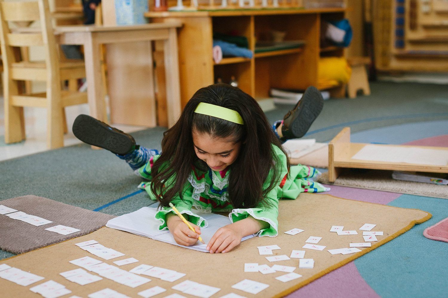 A Montessori child is laying on the floor writing in a notebook.