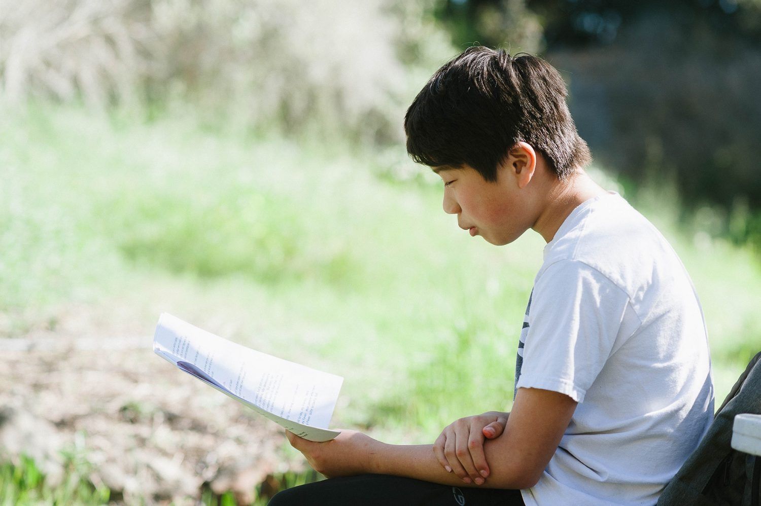 a Montessori child is sitting in a chair outside reading a book